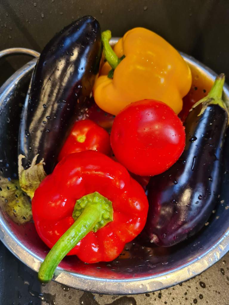 Fresh aubergines, peppers and tomatoes in a colander